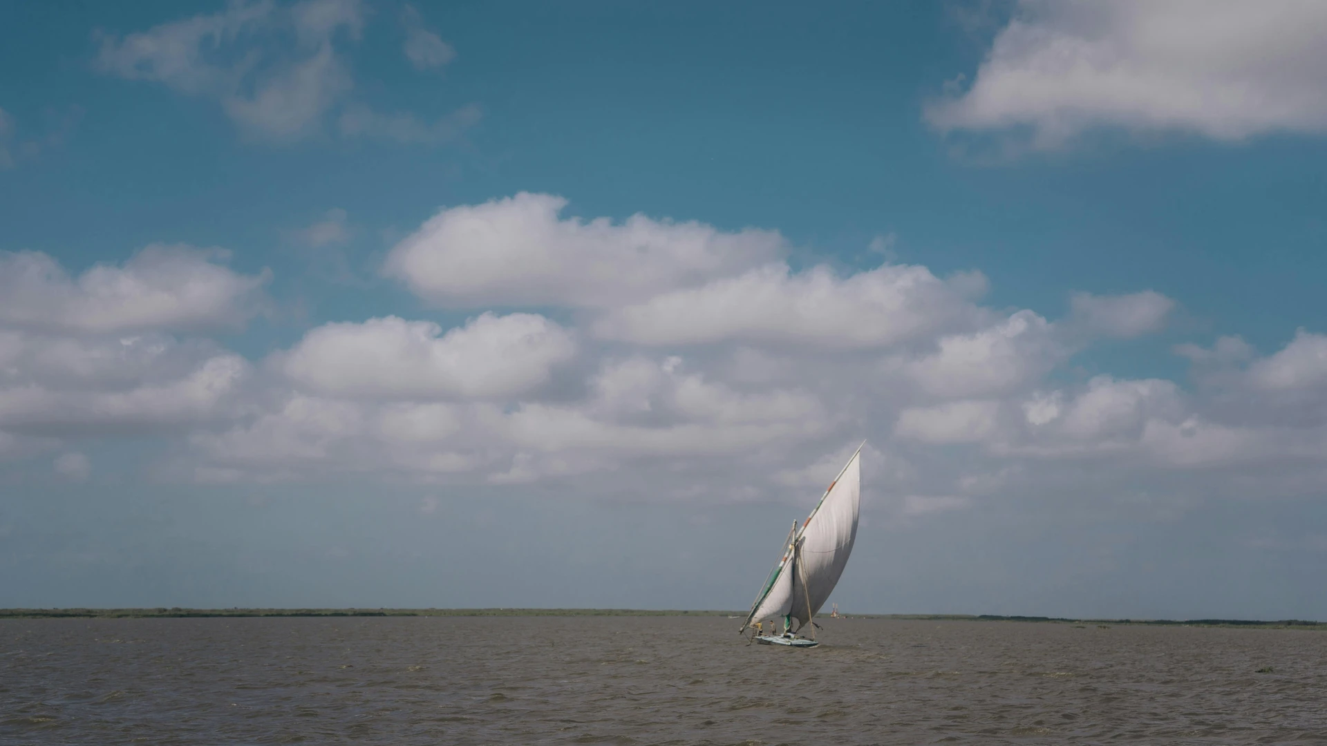 El Gouna, Egypt - Serene view of a sailboat navigating the calm waters with clouds overhead, captured in kafr el-shaikh, egypt.