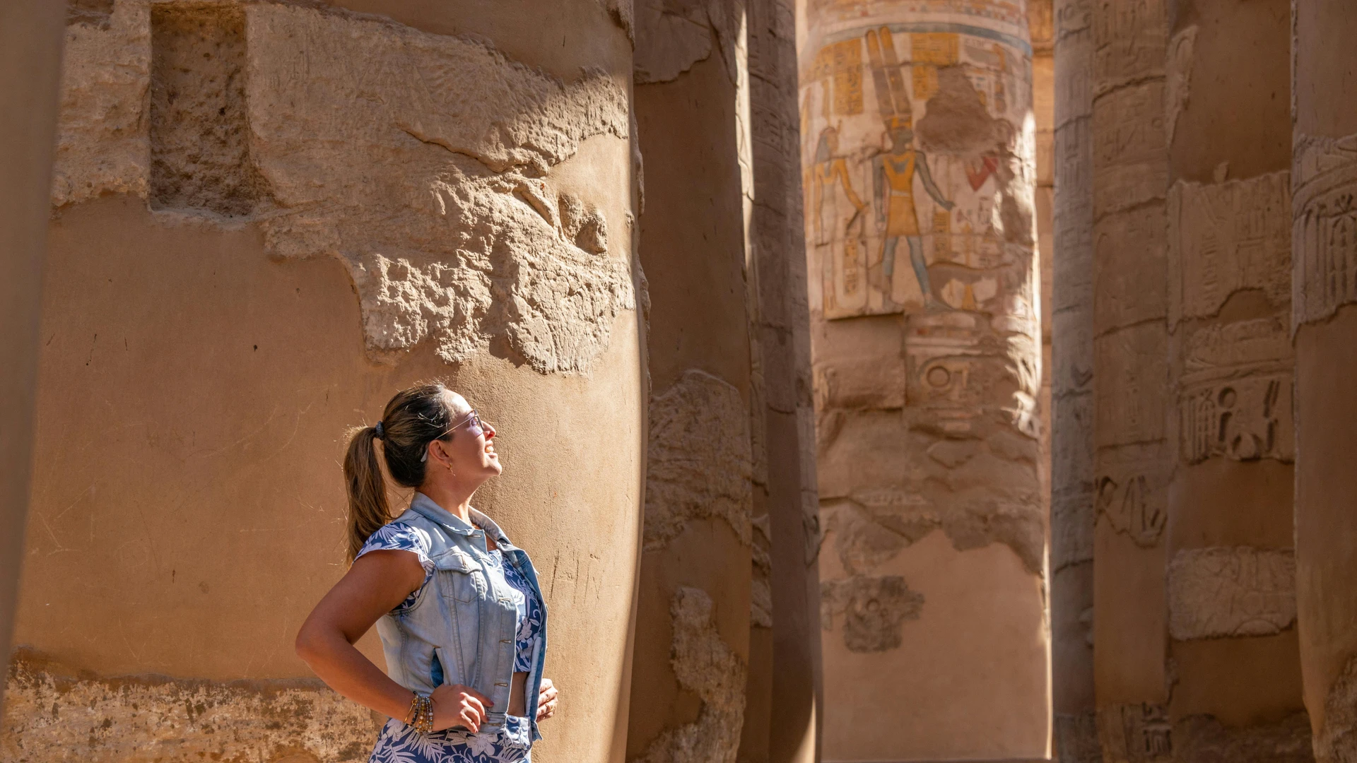 Luxor, Egypt - Woman in luxor temple admiring ancient carved columns in sunlight.
