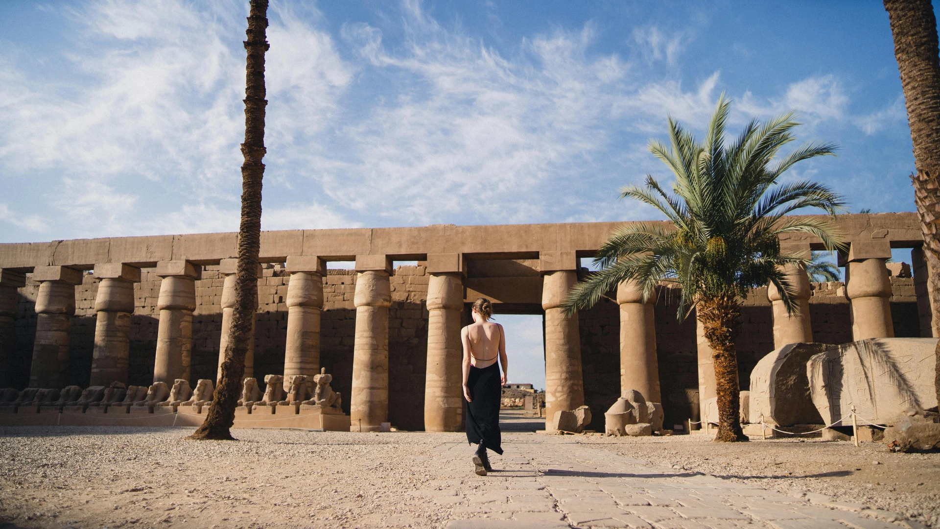 Luxor, Egypt - Woman in a backless black dress walking at the historic karnak temple in egypt.