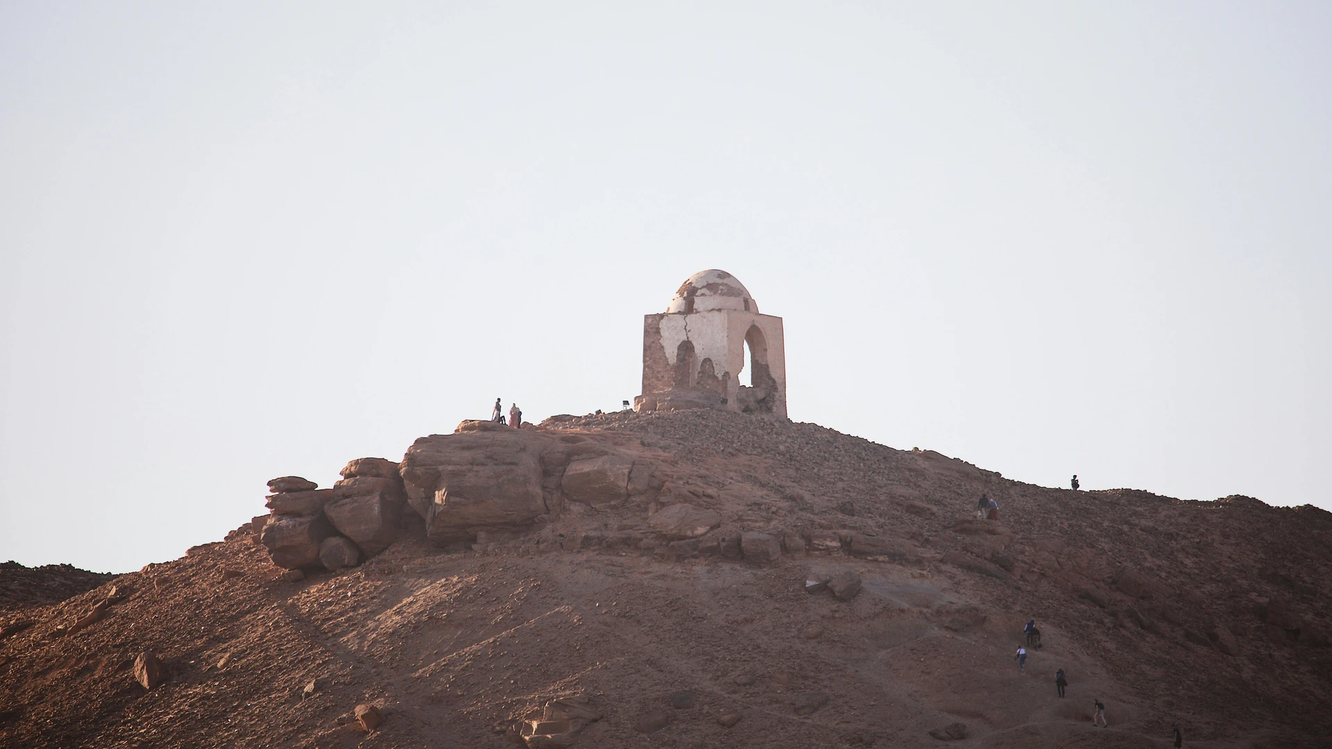 Aswan, Egypt - Silhouetted ancient mausoleum atop a desert hill at sunset in egypt, a serene historical landscape.