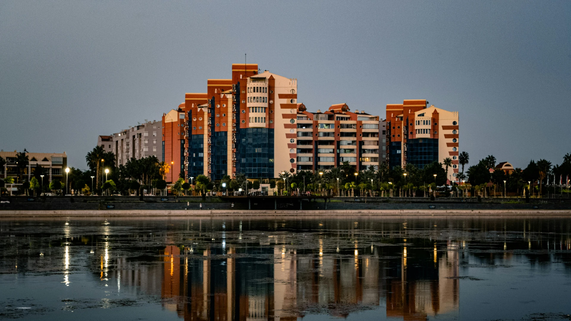 Hurghada, Egypt - Modern cityscape with vibrant building reflections on a calm waterfront at twilight.