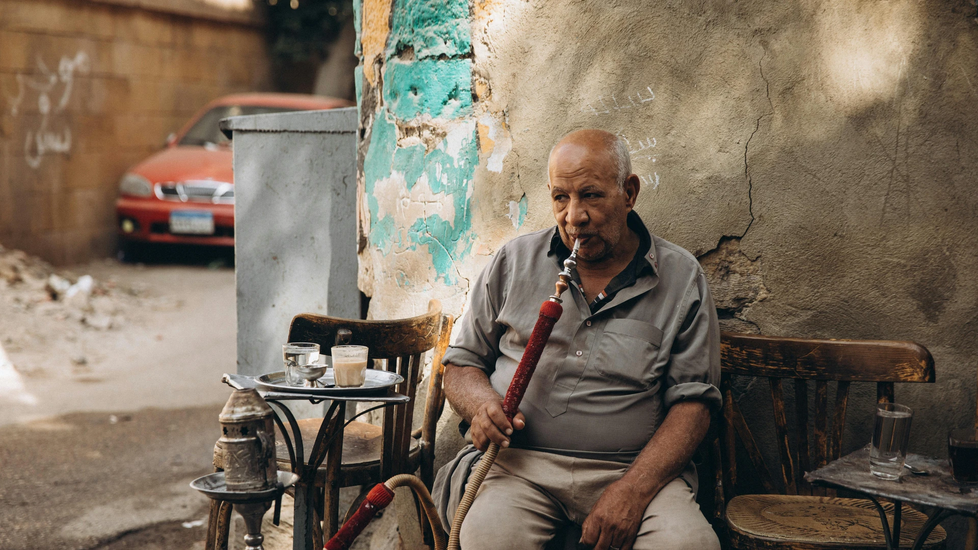 Makadi Bay, Egypt - Elderly man sits outdoors enjoying shisha in cairo, egypt, reflecting local culture.